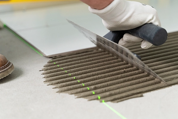 Hand with trowel applying adhesive for tile flooring installation.