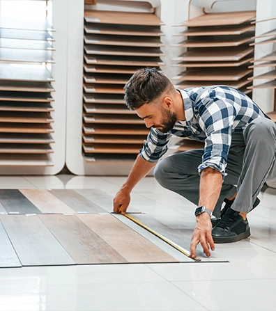 Man measuring wooden panels on showroom floor with a tape measure.