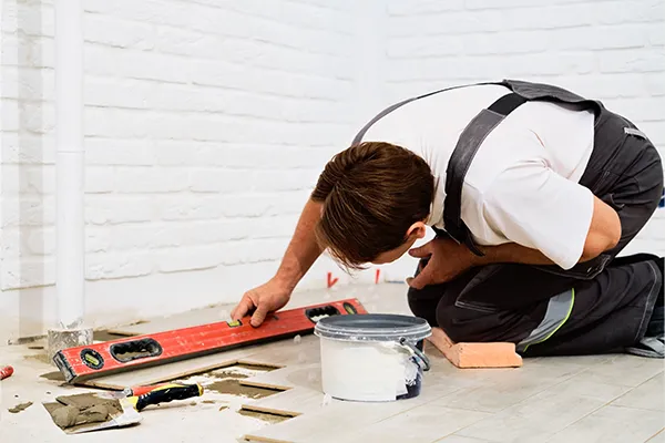 Man kneeling while adjusting floor tiles with a level tool.