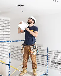 Construction worker on scaffolding inspecting ceiling in brick interior.