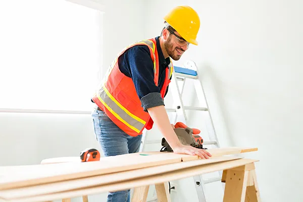 Construction worker using a saw on wooden planks in a bright room.