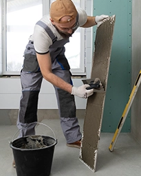 Man applying adhesive on tile in a bright room.