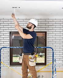 Worker measuring ceiling height with a tape measure in a brick-walled room.