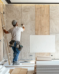 Worker installing wooden panels on an unfinished interior wall.